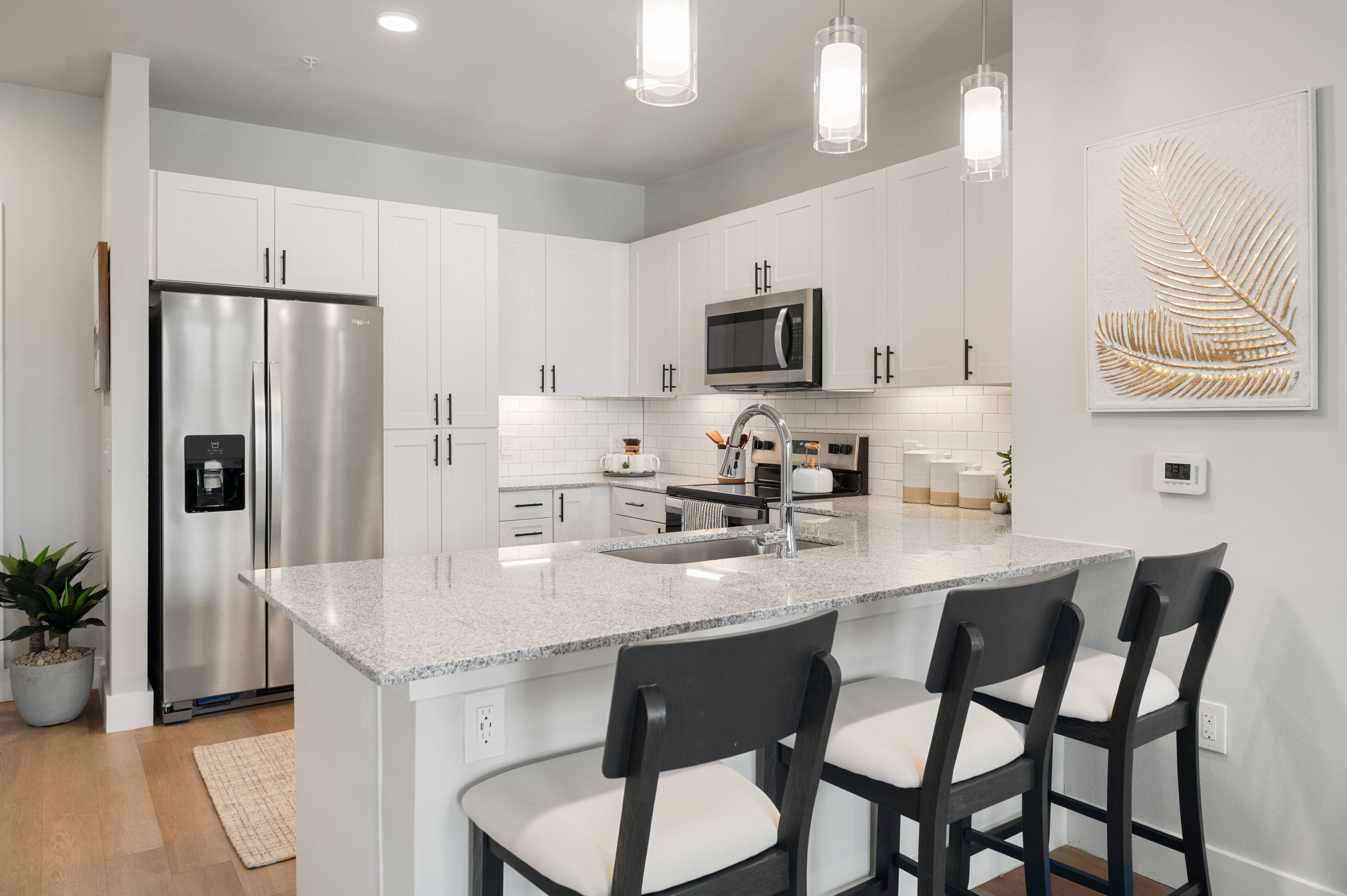 A kitchen with a refrigerator, microwave, and a counter with chairs.